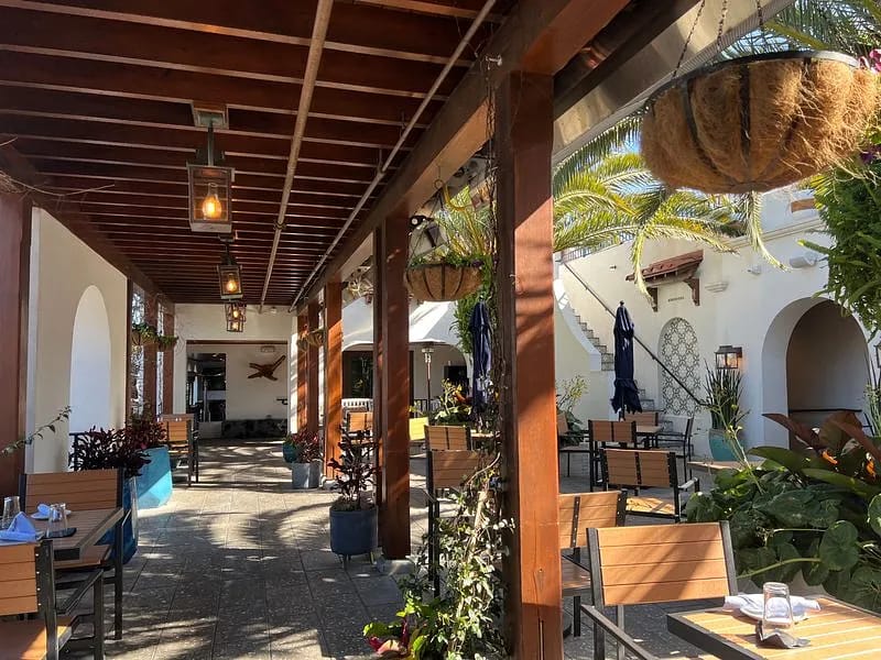 Patio with wooden beams, tile floor, tables, chairs, potted plants, and hanging planters.
