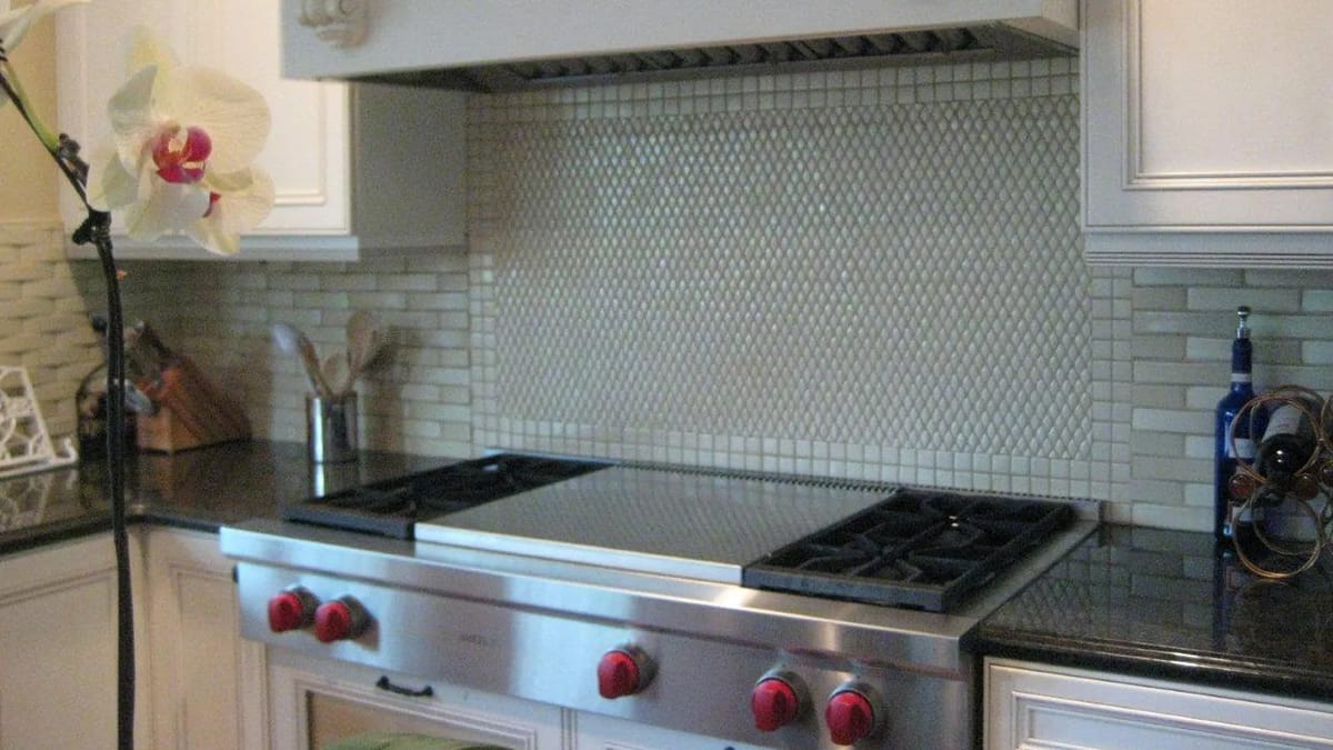Kitchen with stainless steel range, red knobs, mosaic tile backsplash, and dark granite countertops.