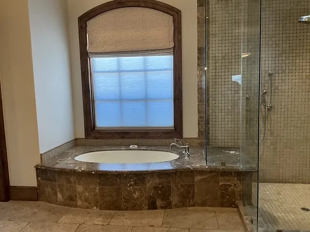 Bathroom with freestanding tub, tiled shower, and large window with wooden frame.