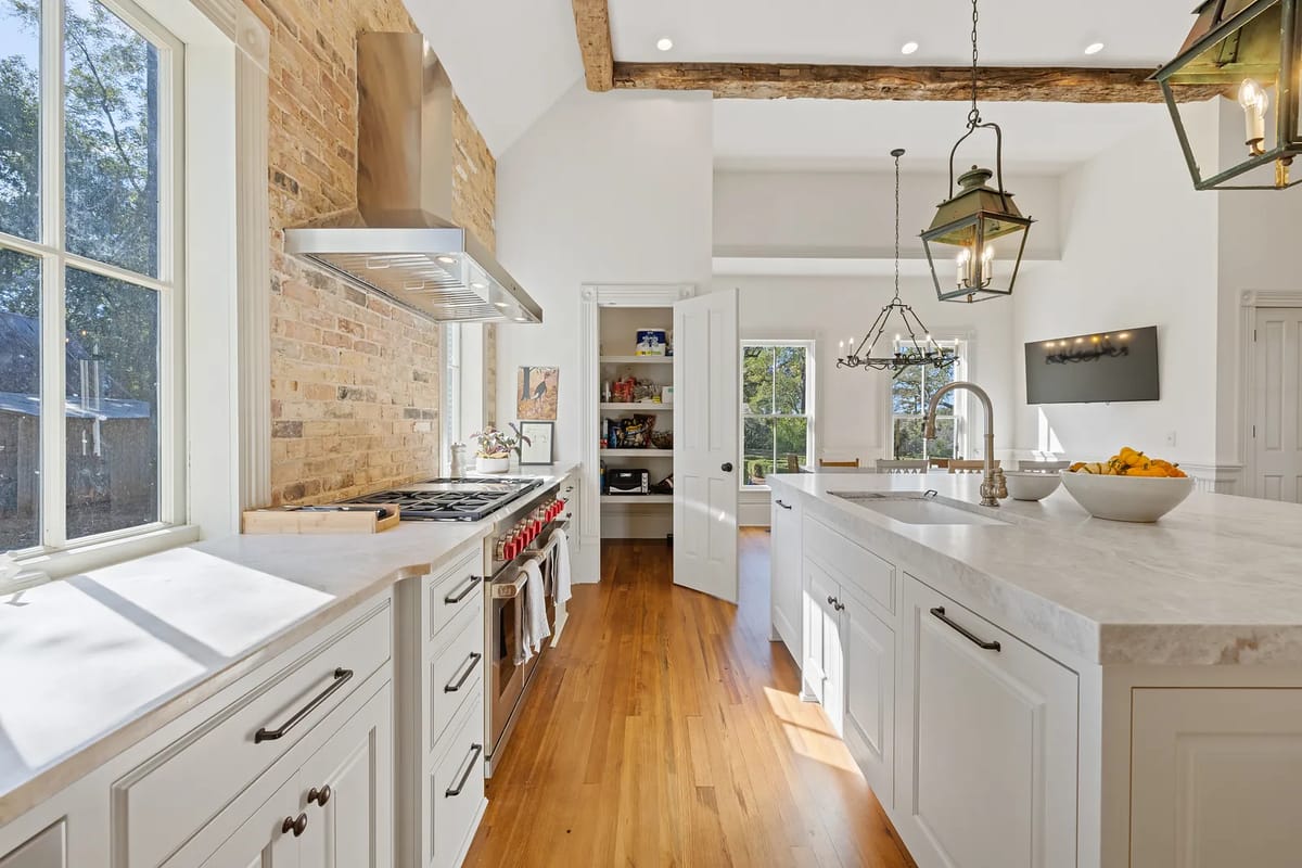 Kitchen with marble island, gas stove, wood cabinets, exposed beams, and pendant lights.