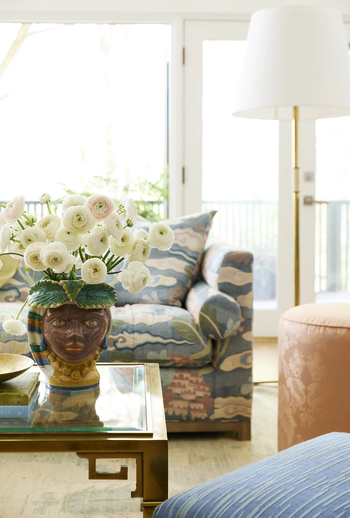 Living room with patterned sofa, coffee table, flowers, and sliding door to outdoor area.