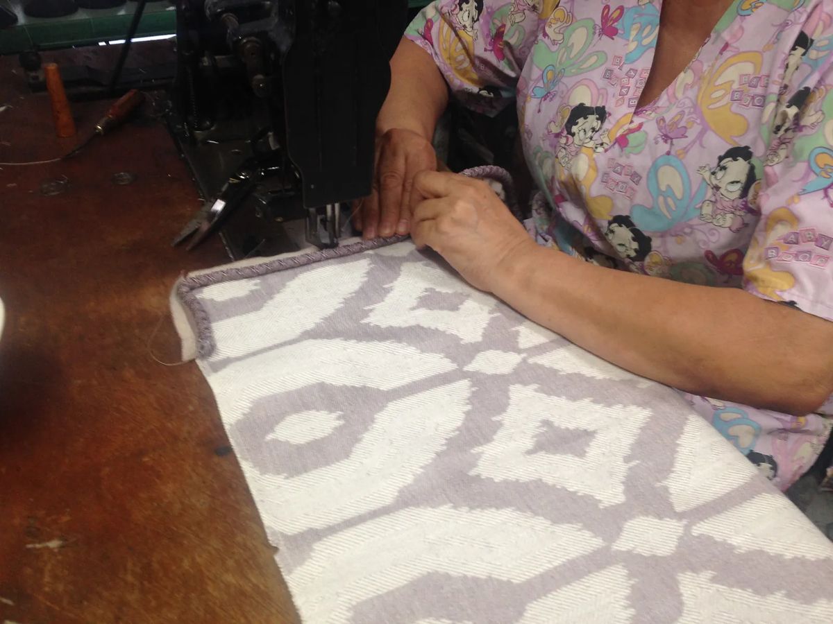 Person sewing fabric on a machine at a wooden table with sewing tools.