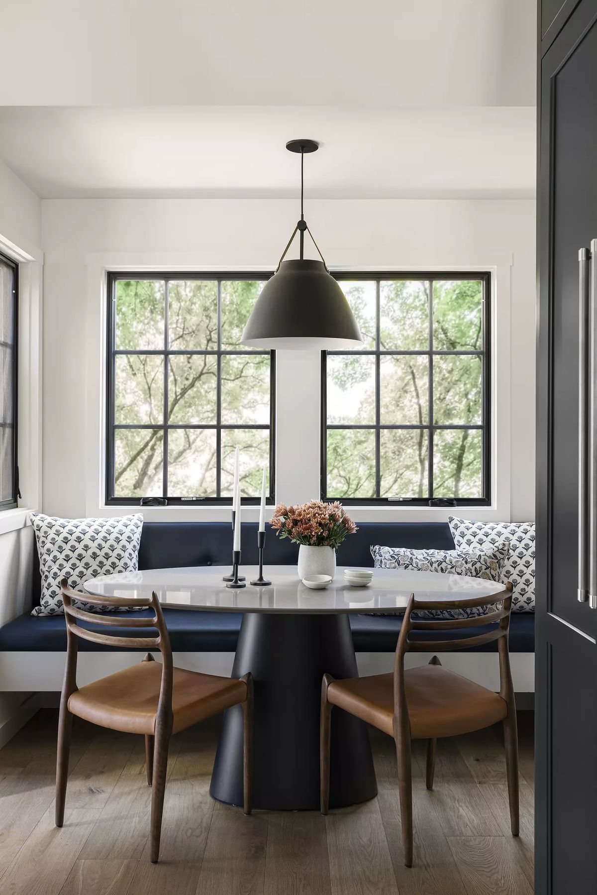 Dining room with round table, wooden chairs, built-in bench, and large windows for views of greenery.