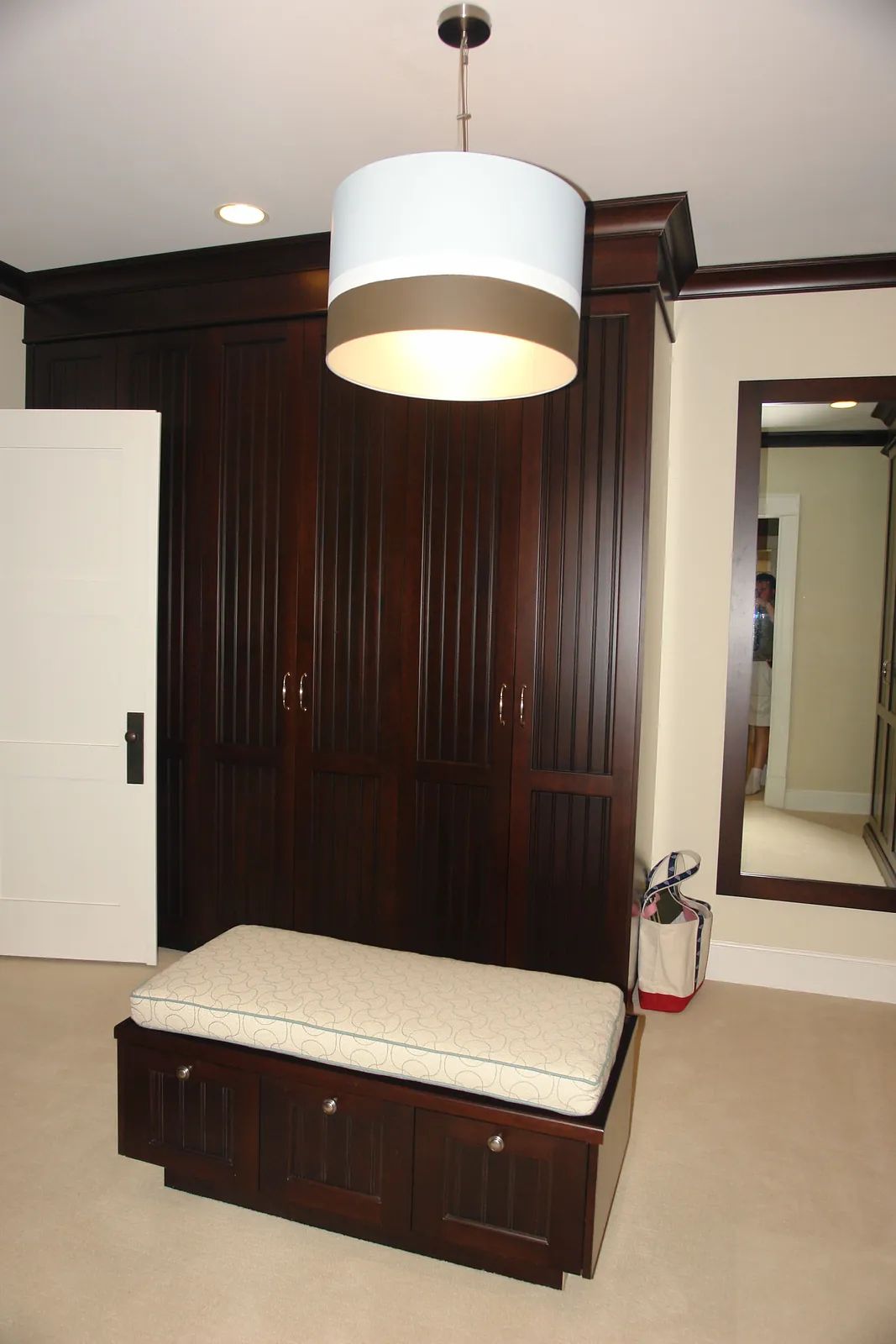 Mudroom with dark wooden storage, white bench, large mirror, and light-colored carpet