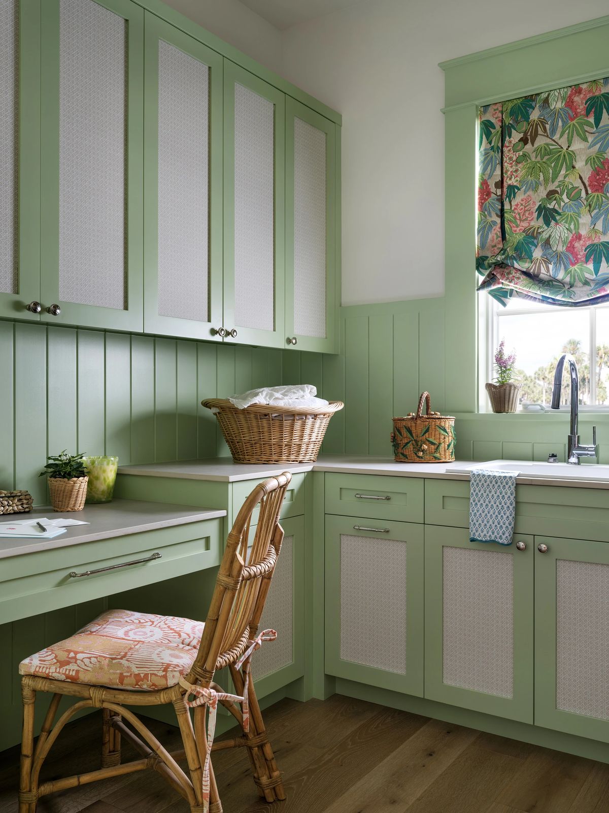 Laundry room with green cabinetry, countertop, wicker basket, and floral curtain at the window.