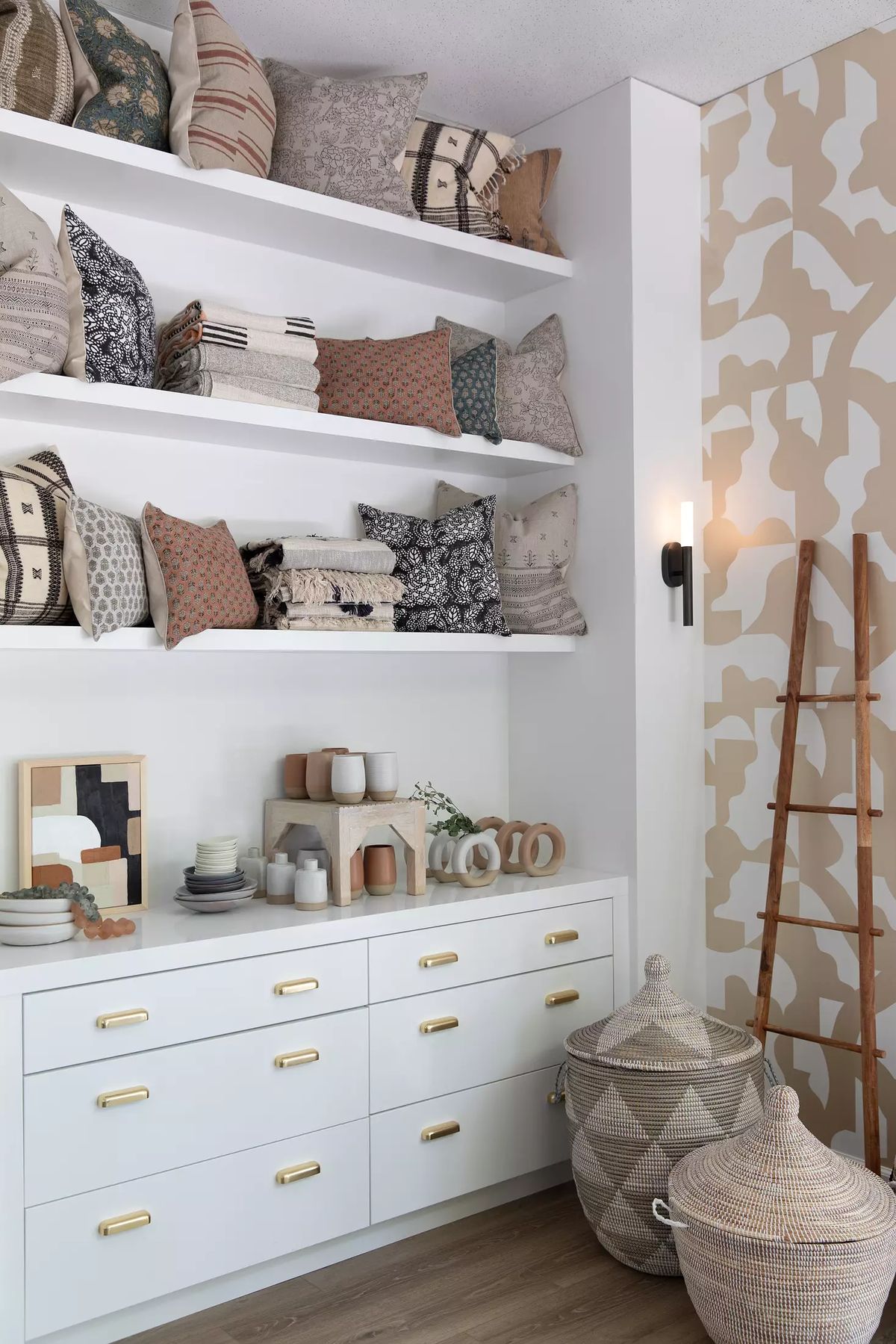 Space with floating shelves, white dresser, patterned pillows, vase, and woven baskets on the floor.