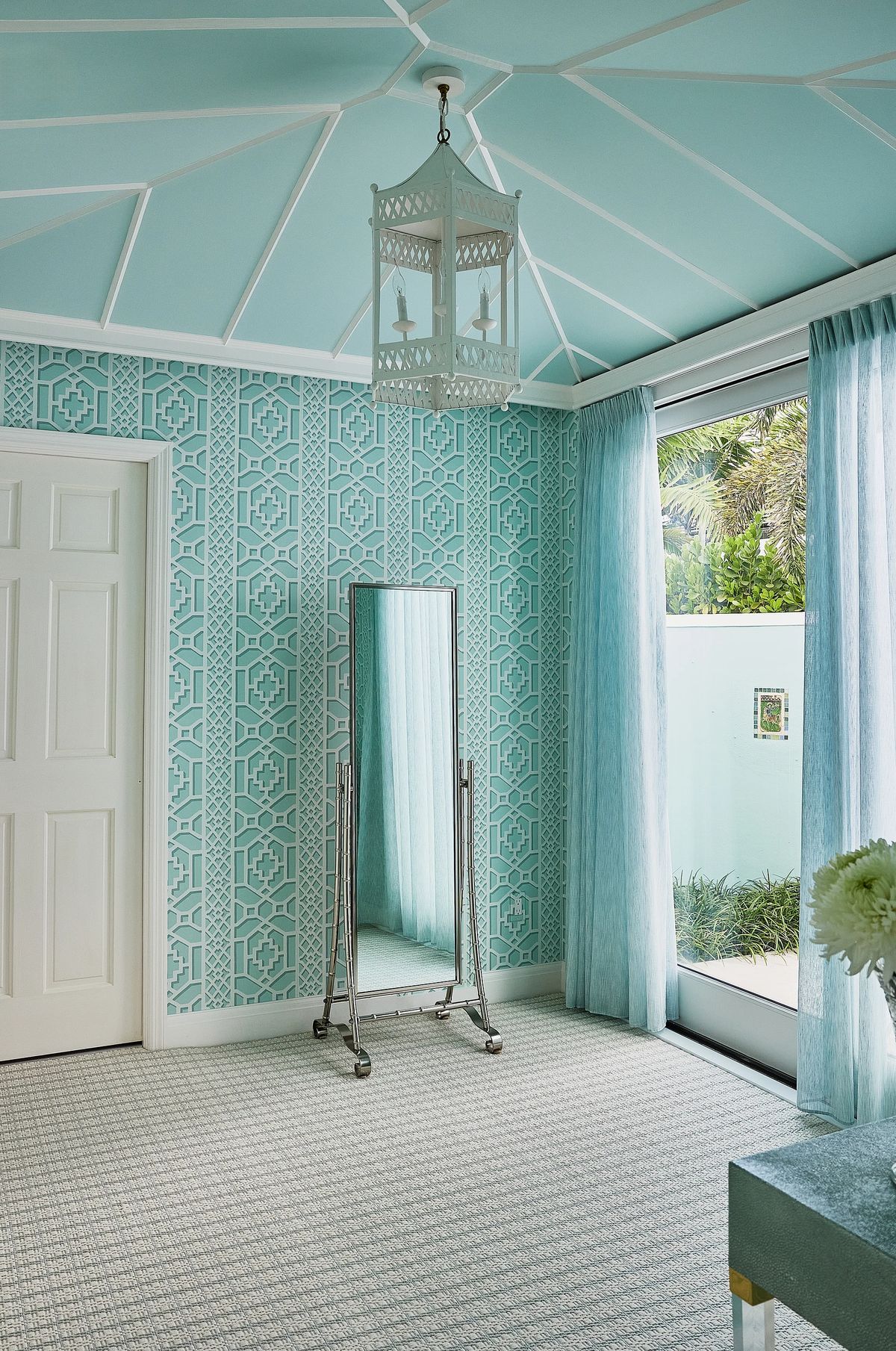 Room with turquoise geometric wallpaper, full-length mirror, blue curtains, and a textured gray carpet.