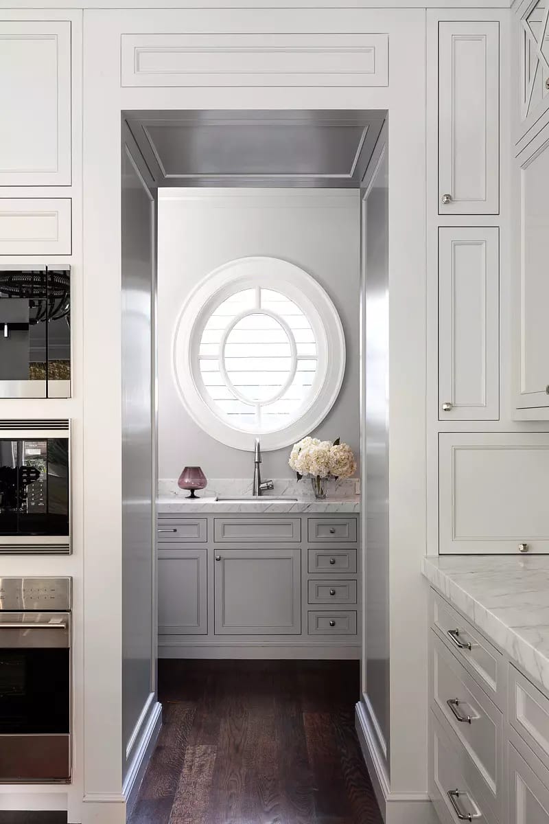 Kitchen with white cabinetry, circular window, marble countertop, stainless steel appliances, and decorative flowers