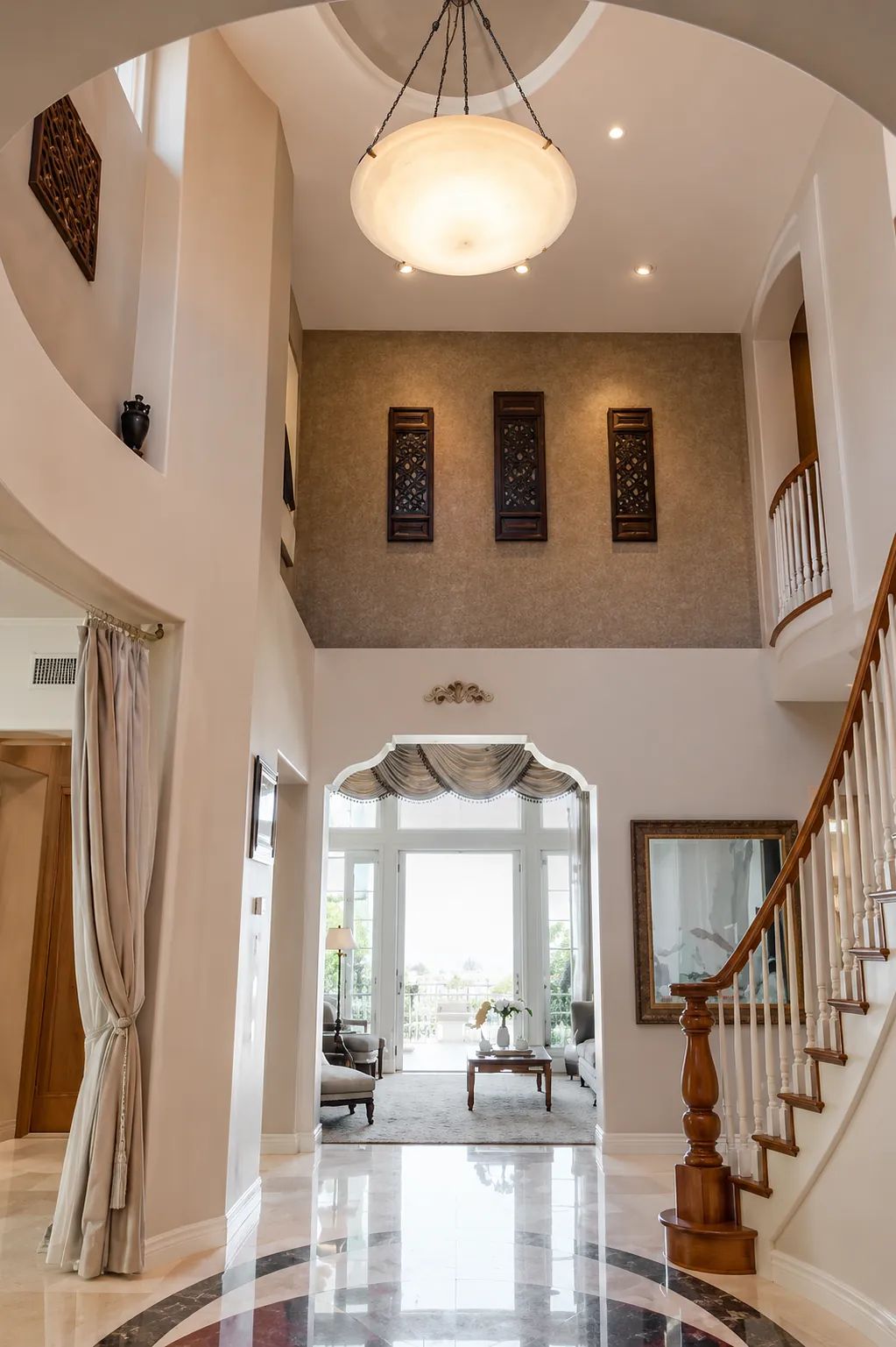 Foyer with marble floor, curved staircase, artwork, and large light fixture with tall windows.