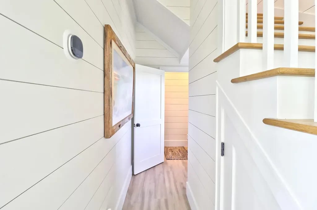 Hallway with shiplap walls, wooden staircase, door, and framed picture.