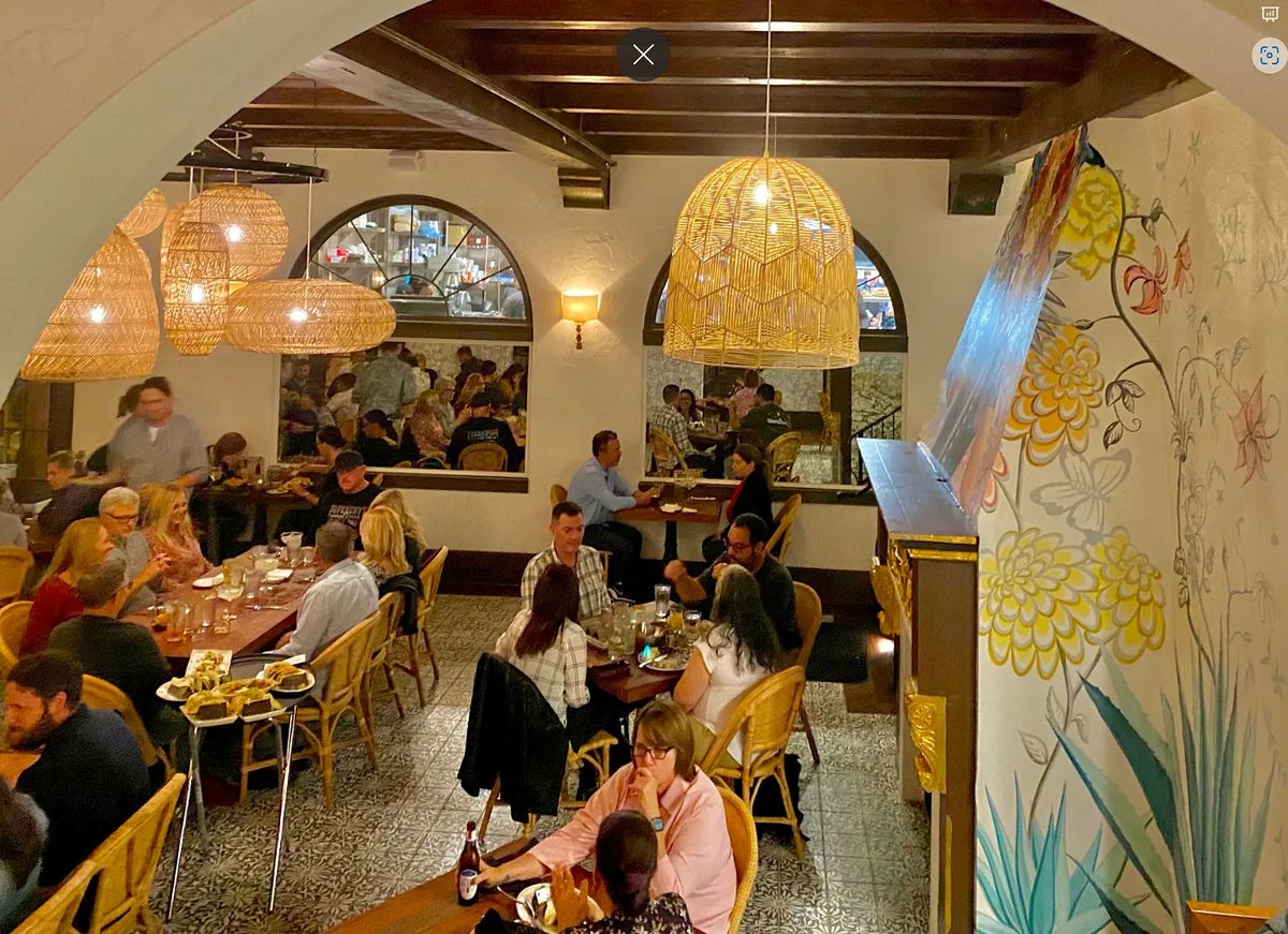 Dining room with tables, woven chairs, pendant lights, and patterned wallpaper.