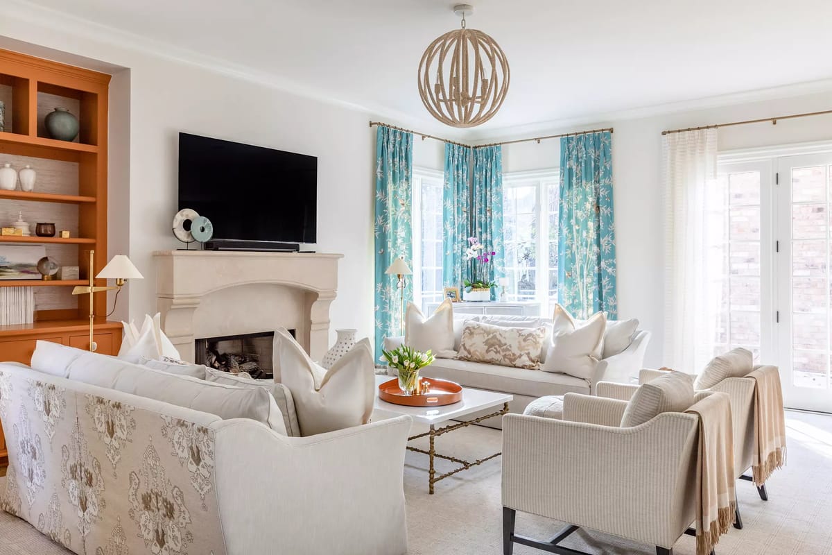 Living room with sofas, coffee table, armchairs, built-in bookshelves, television, windows, and floral curtains