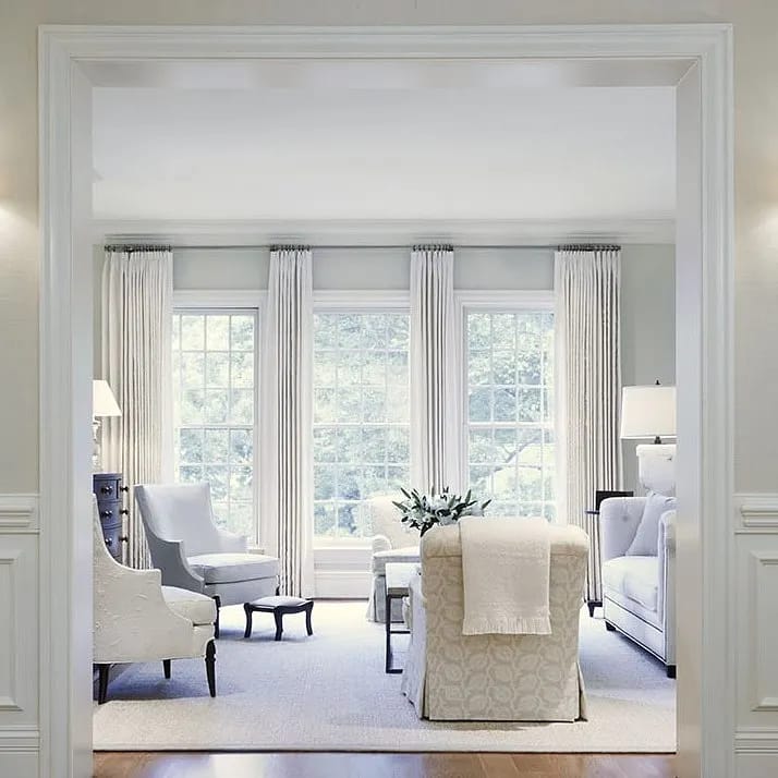 Living room with white sofa, gray armchairs, coffee table, area rug, large windows, and wainscoting.