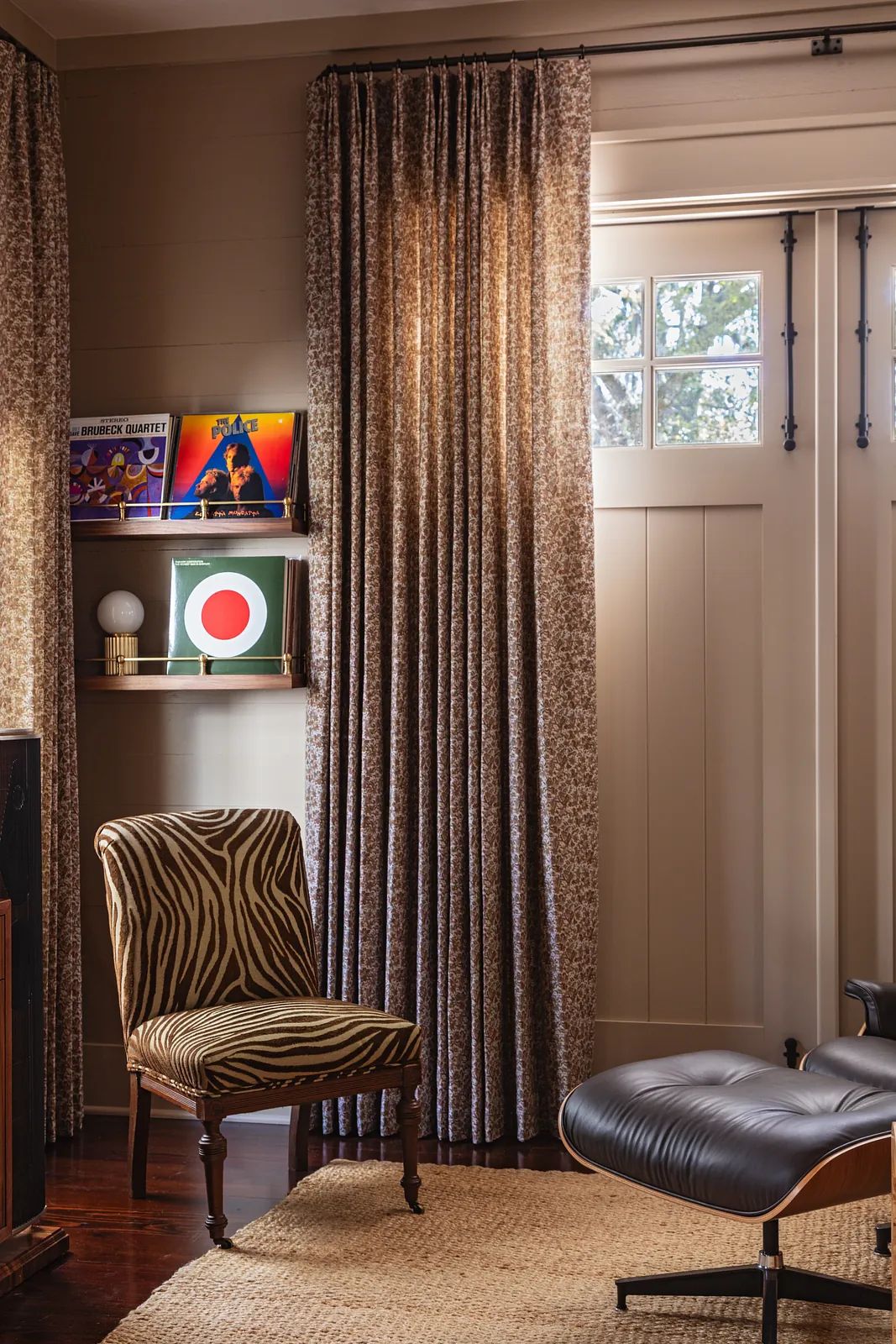 Living room corner with zebra-striped chair, black leather lounge chair, woven rug, and decorative shelves.