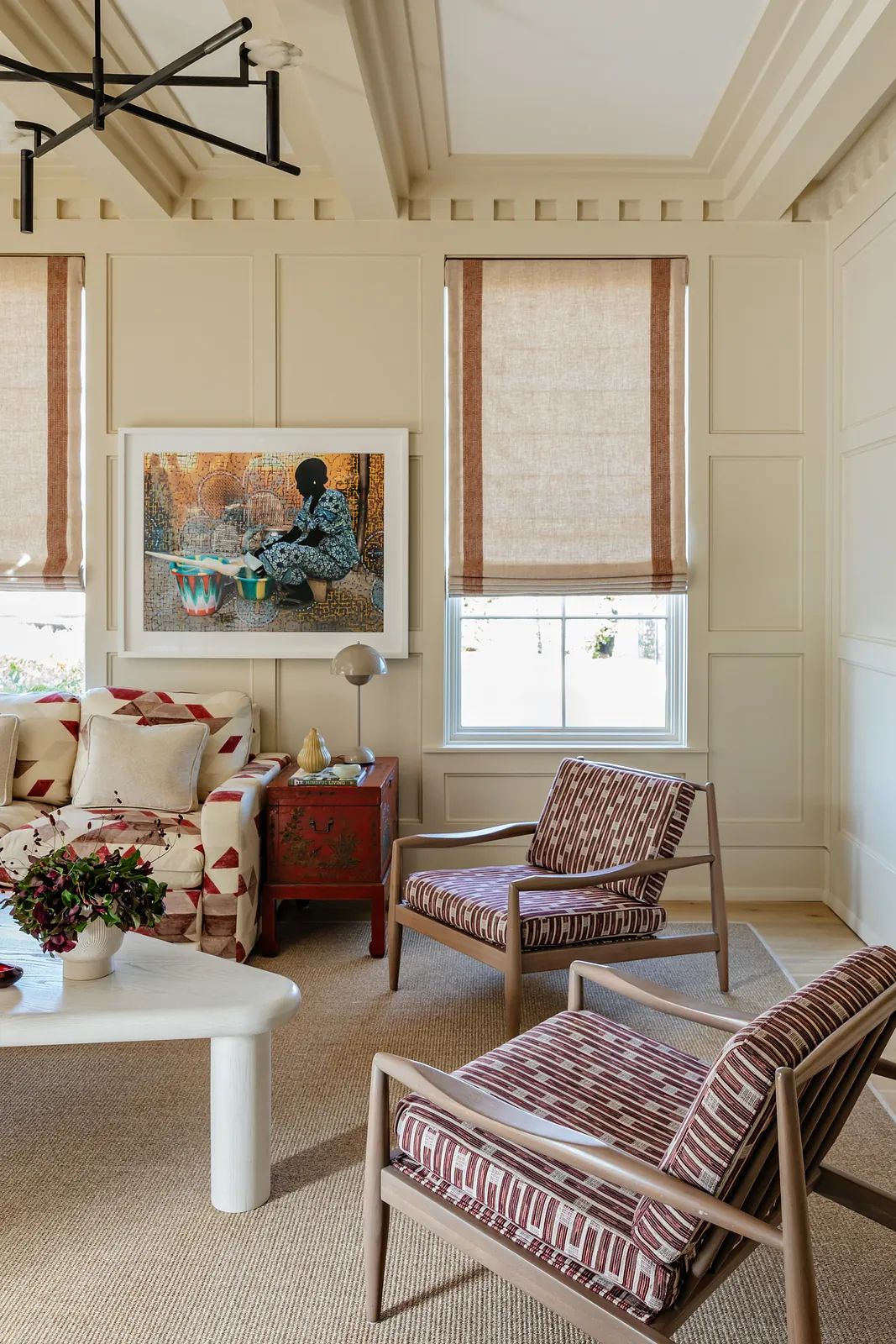Living room with patterned sofa, striped chairs, white coffee table, and artwork on paneled walls.