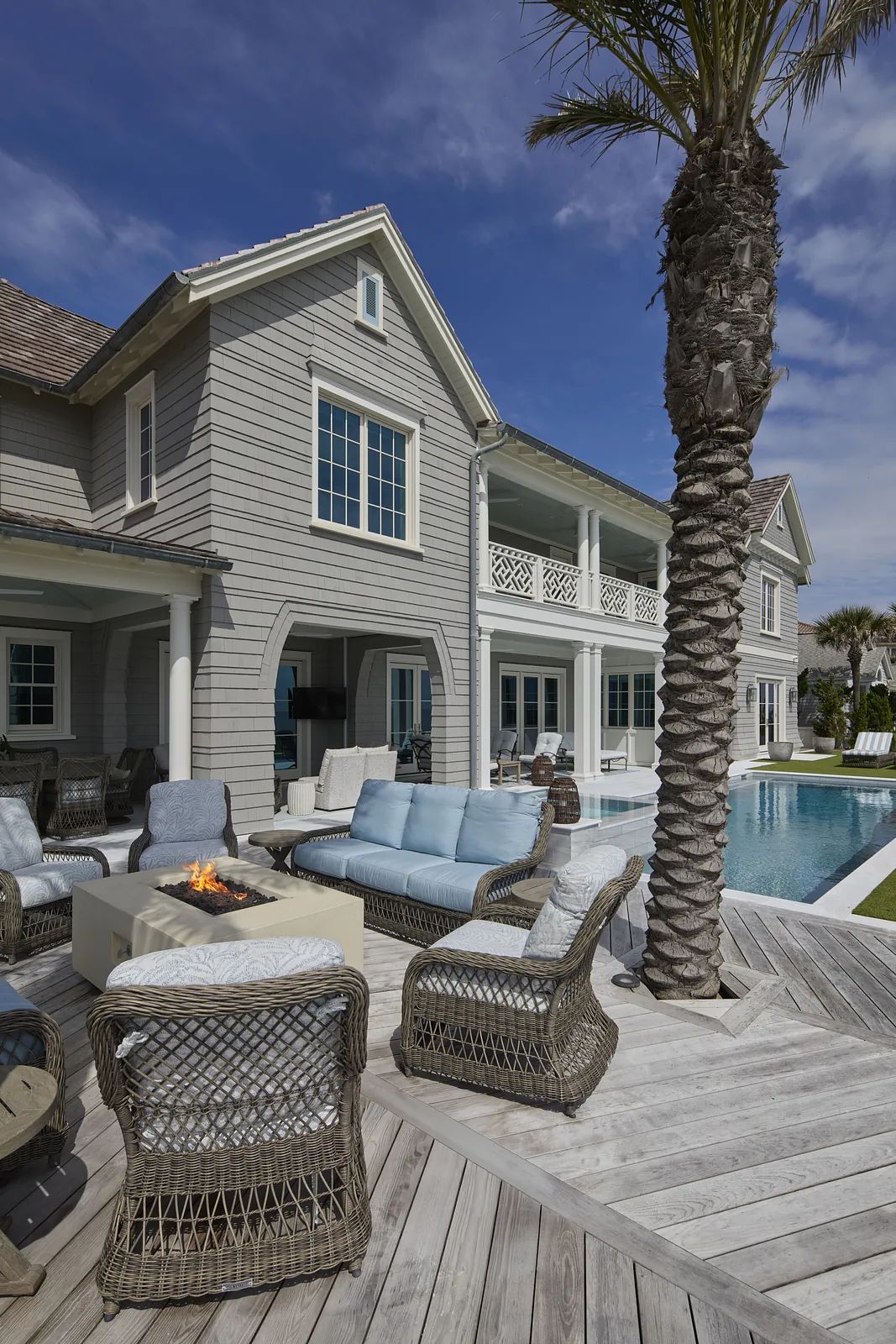 Patio with wicker seating, fire pit table, pool, palm trees, and wooden deck.