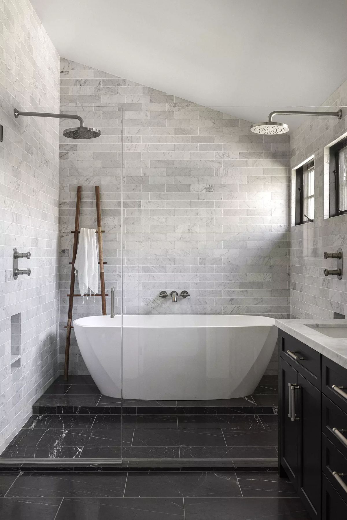 Bathroom with freestanding bathtub, glass shower, gray stone tile, and wooden towel ladder