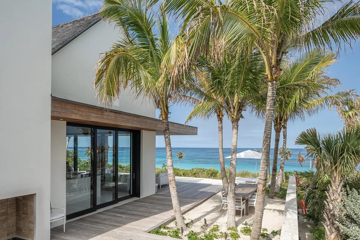 Beachfront exterior with palm trees, wooden deck, glass doors, and ocean view.