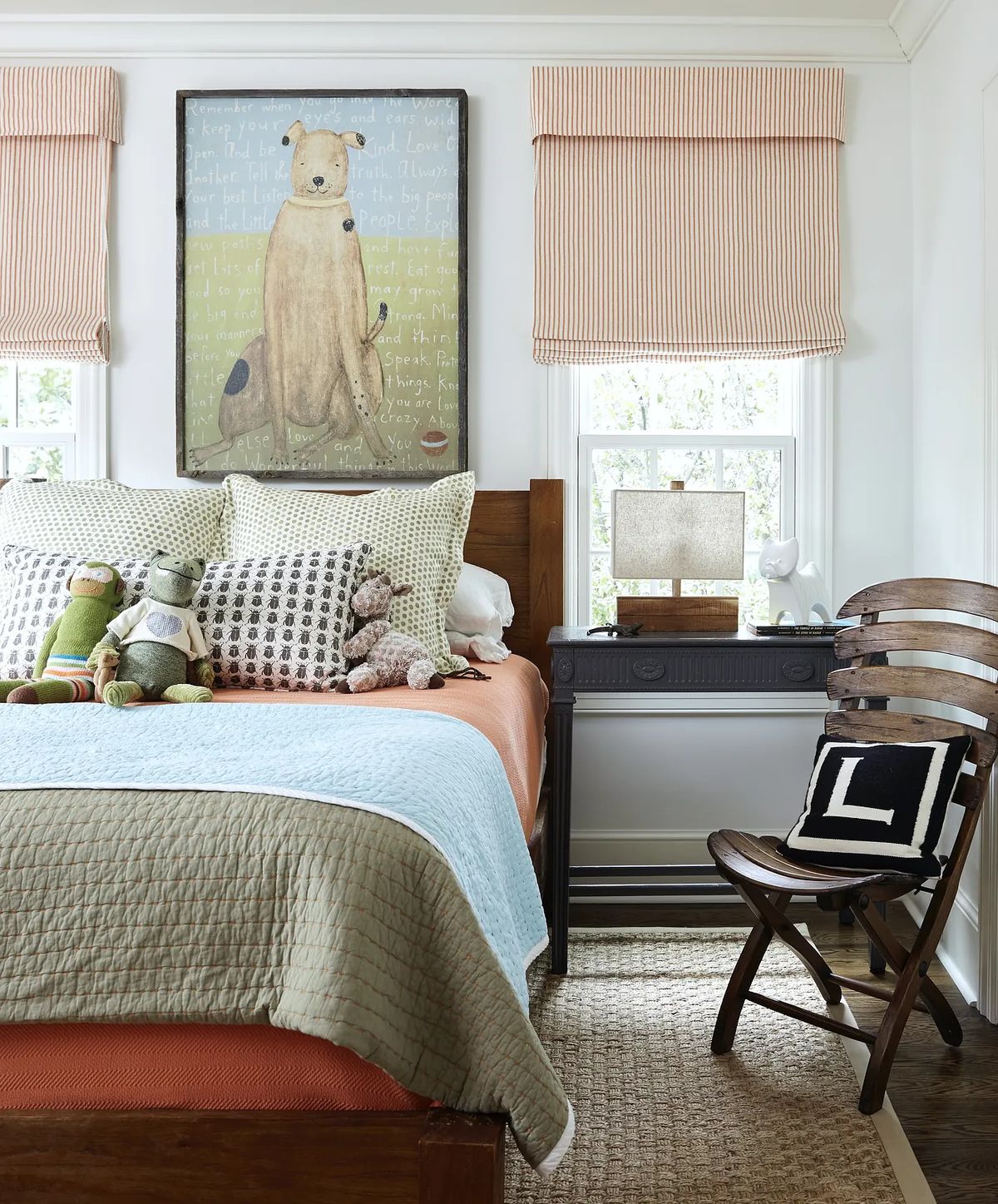 Bedroom with wooden bed, orange and blue quilt, decorative pillows, art, desk, chair, and striped window shades