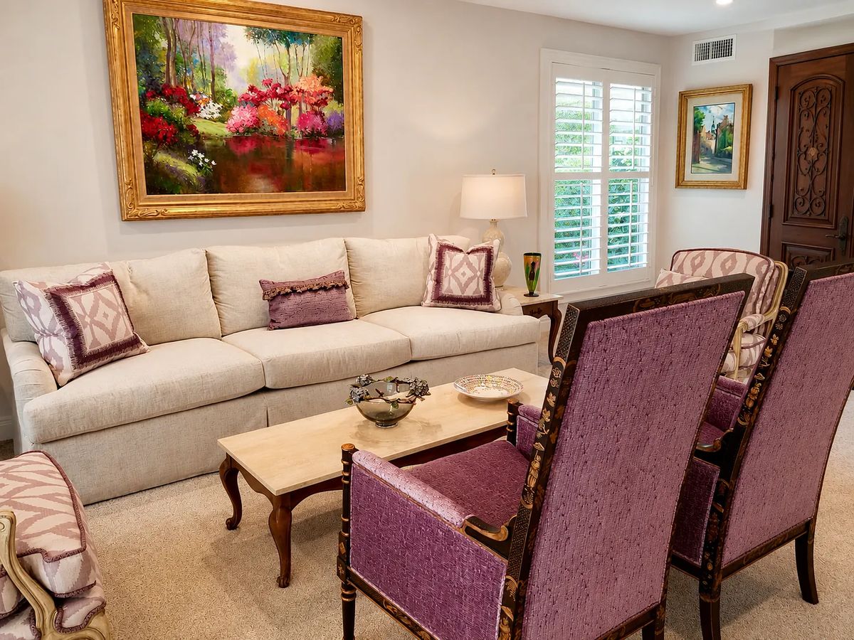 Living room with light sofa, patterned armchairs, coffee table, flower painting, and decorative artwork.