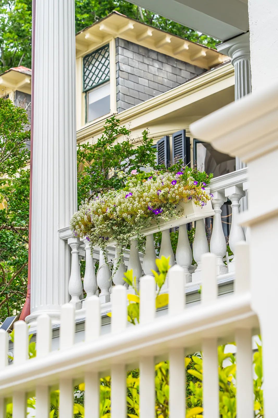 Exterior front view with white picket fence, flower boxes, columns, shingled facade, and window shutters.