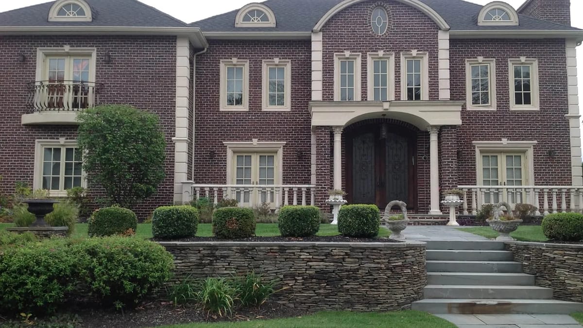 Front exterior of a brick house with double doors, stone steps, windows, and landscaped yard.