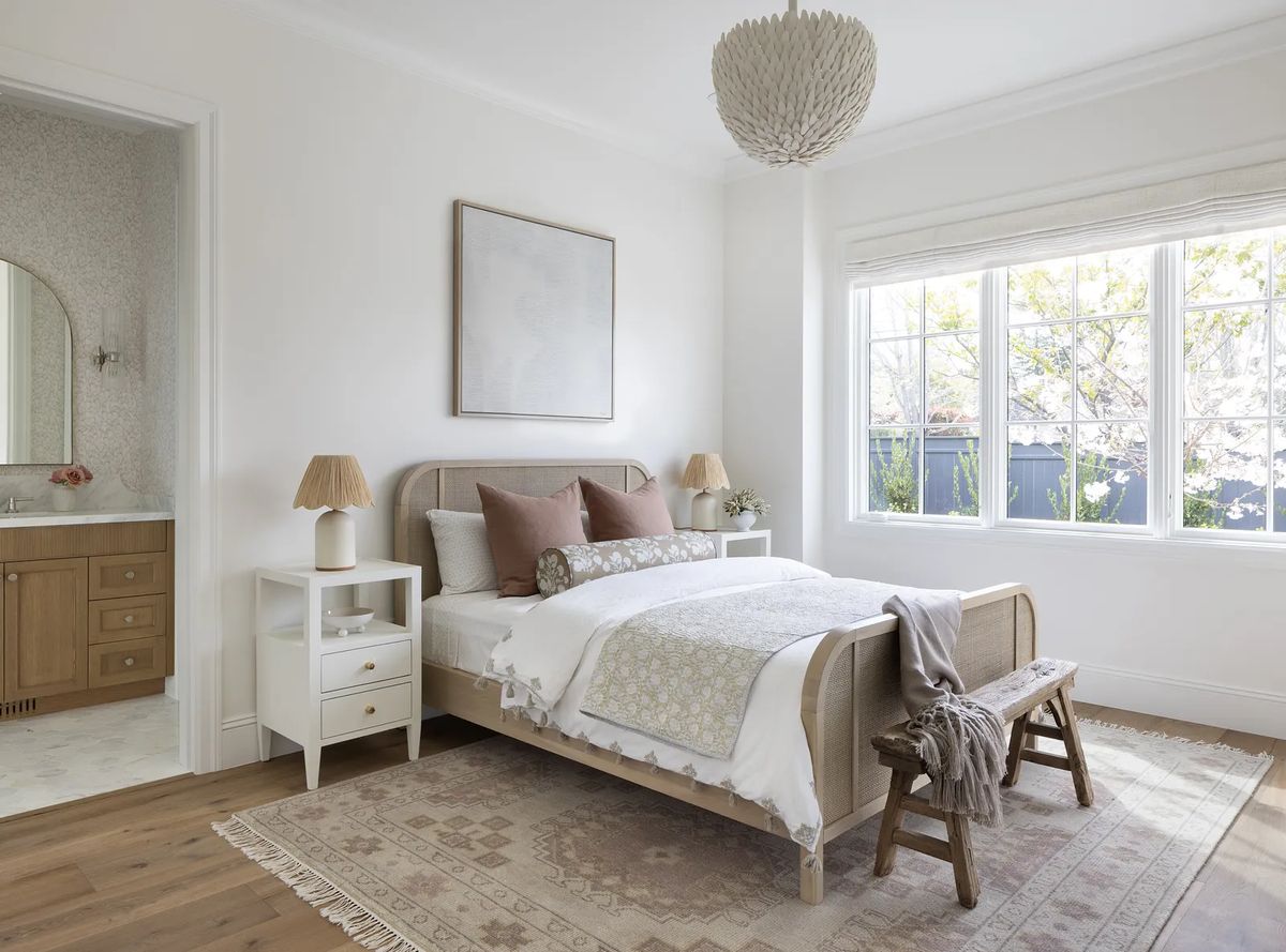 Bedroom with light bed frame, gray bedding, nightstands, bench, and large window with natural light.
