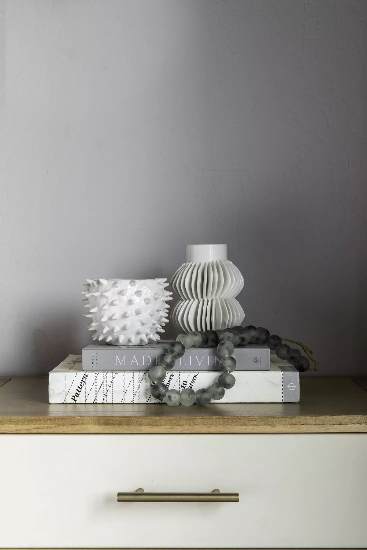 Tabletop display with spiked bowl, pleated vase, books, and decorative beads on a wooden surface.