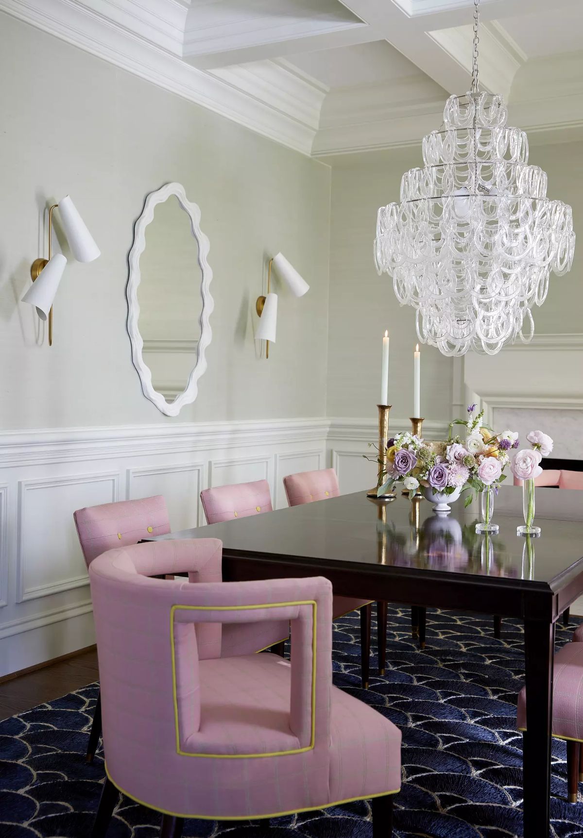 Dining room with dark wood table, pink chairs, crystal chandelier, and floral arrangement.
