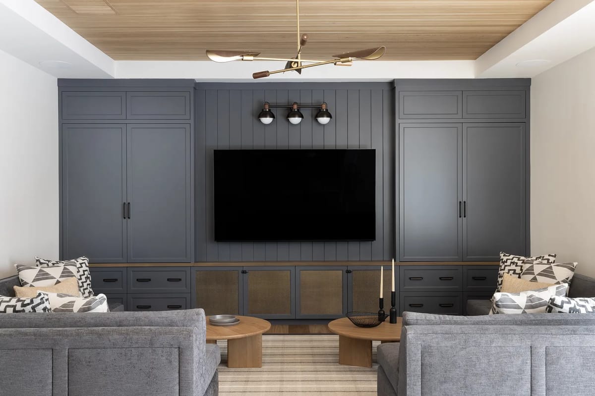 Living room with gray sofas, central coffee table, dark cabinetry, stripes rug, and wood-paneled ceiling