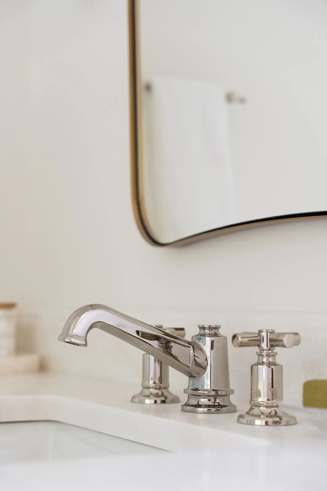 Bathroom sink area with chrome faucet, two handles, mirror, and white sink surface.