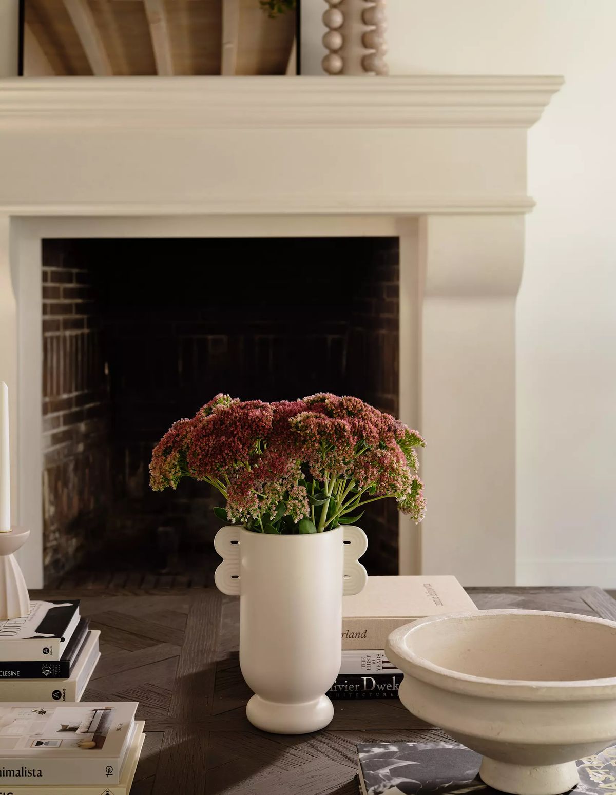 Living room with mantel, fireplace, white vase, books, and round bowl on wood table.
