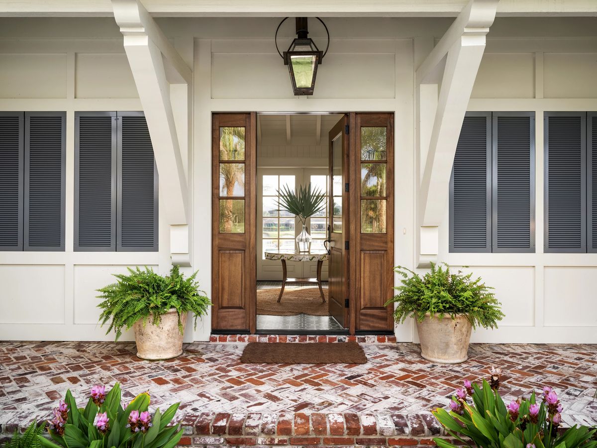 Exterior front with double door entrance, potted ferns, flowering plants, and red brick flooring.