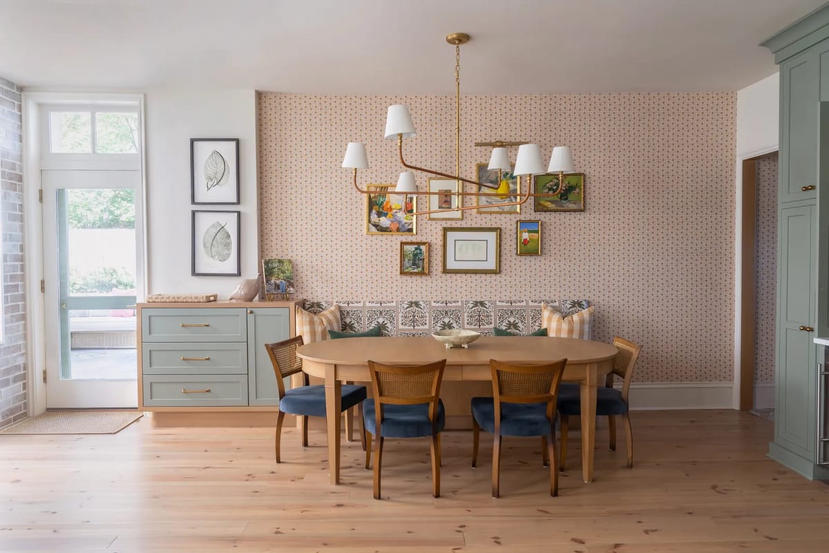 Dining room with round wooden table, blue chairs, artwork, gray cabinets, and patterned wallpaper.