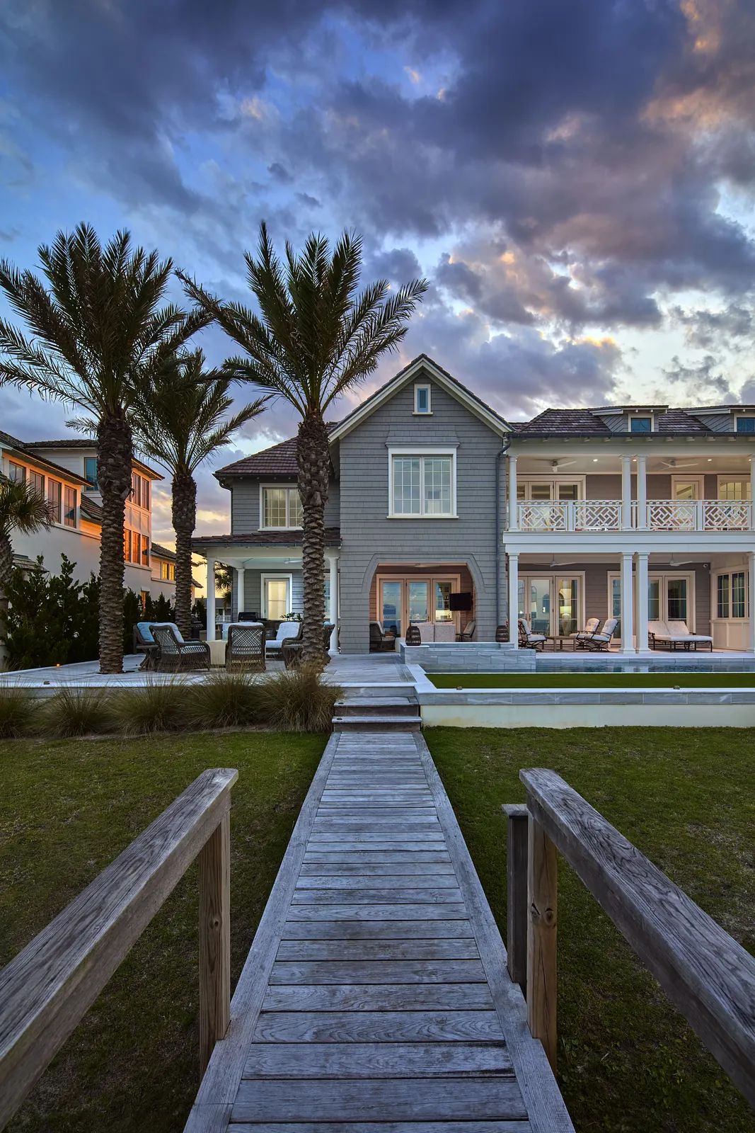Exterior rear of a house with walkway, pool, palm trees, and gray facade.