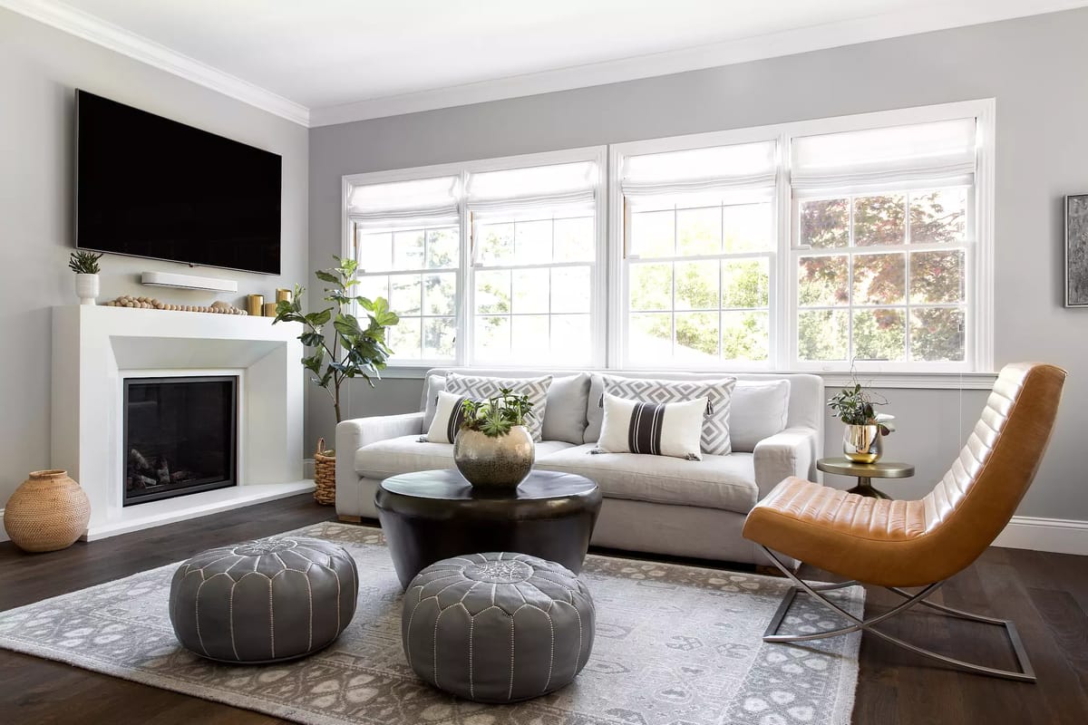 Living room with white sofa, black coffee table, poufs, large windows, and a fireplace.