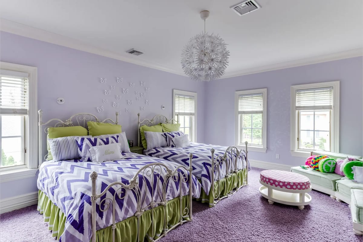 Bedroom with twin beds, purple and green bedding, pink ottoman, and lavender walls with butterfly decor.