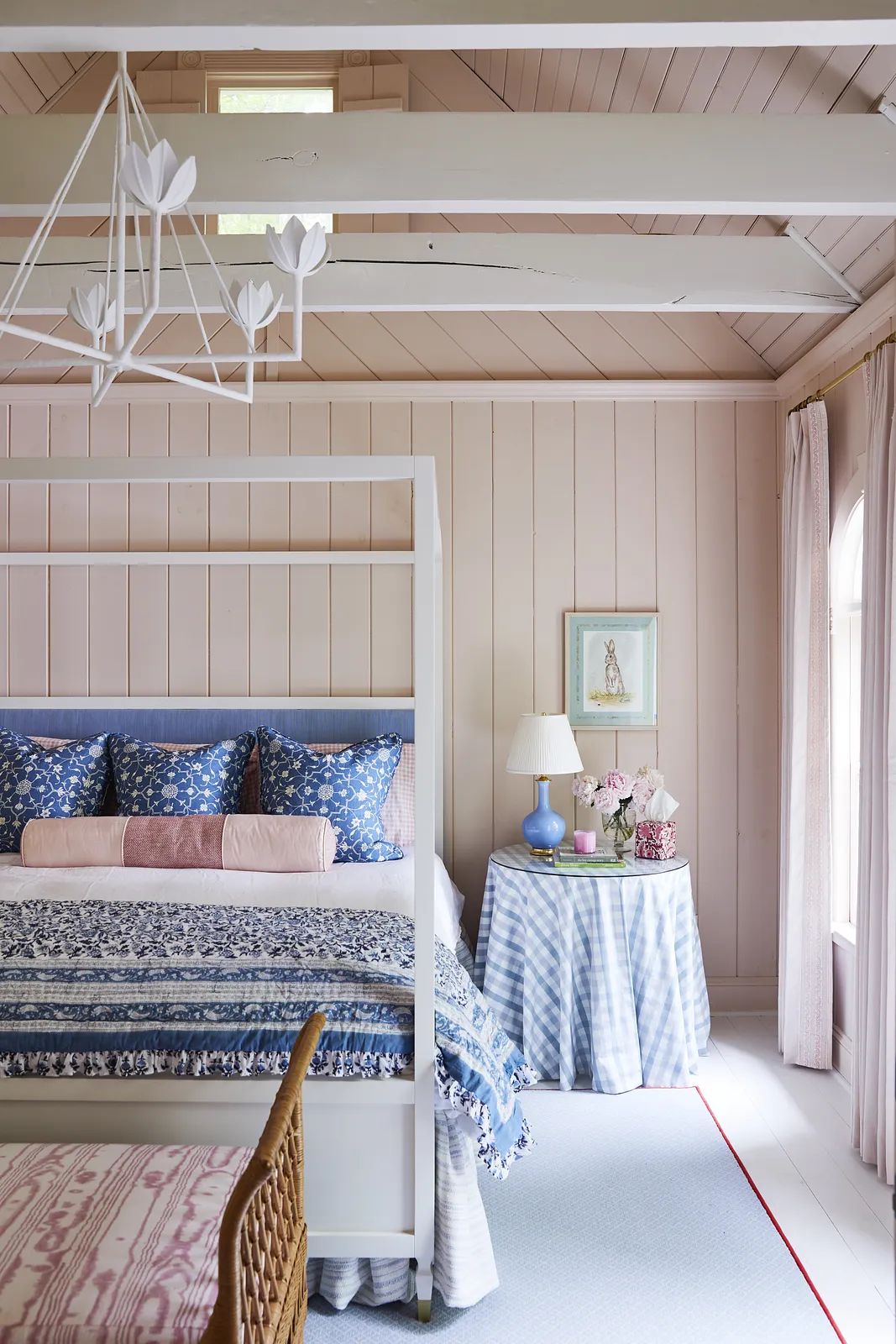 Bedroom with canopy bed, blue bedding, round table with lamp, and light pink paneling