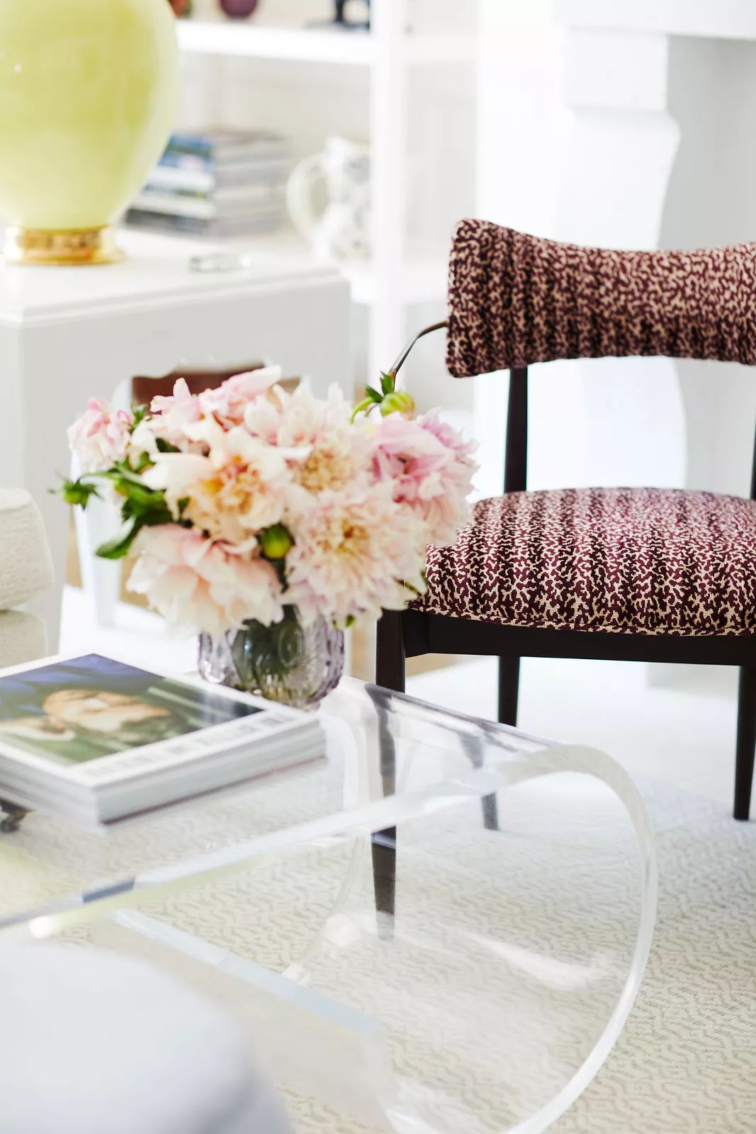 Living room with acrylic coffee table, patterned chair, floral arrangement, and magazines on the table.