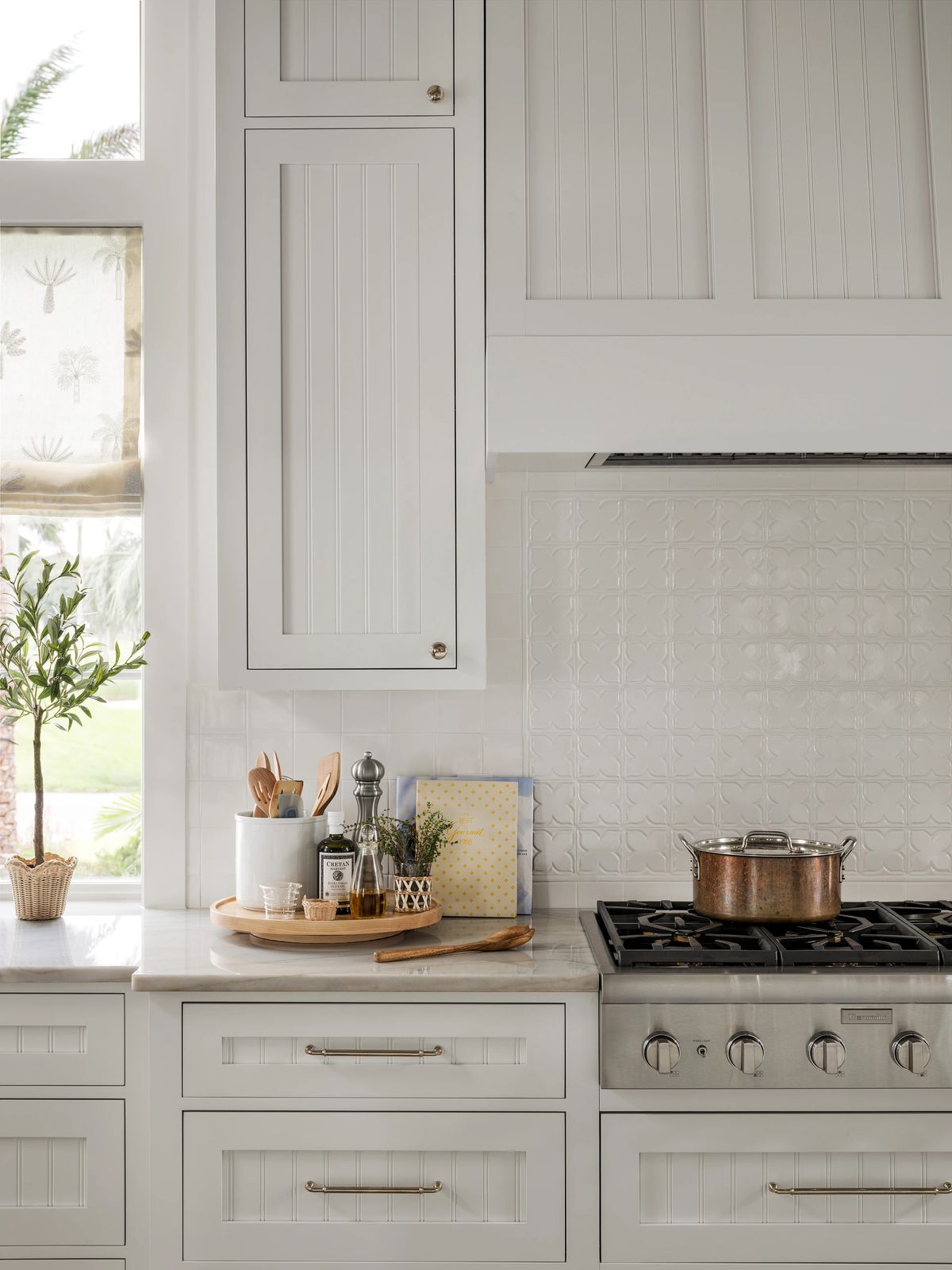 Kitchen with white cabinetry, gas range, marble countertop, and window with fabric curtains