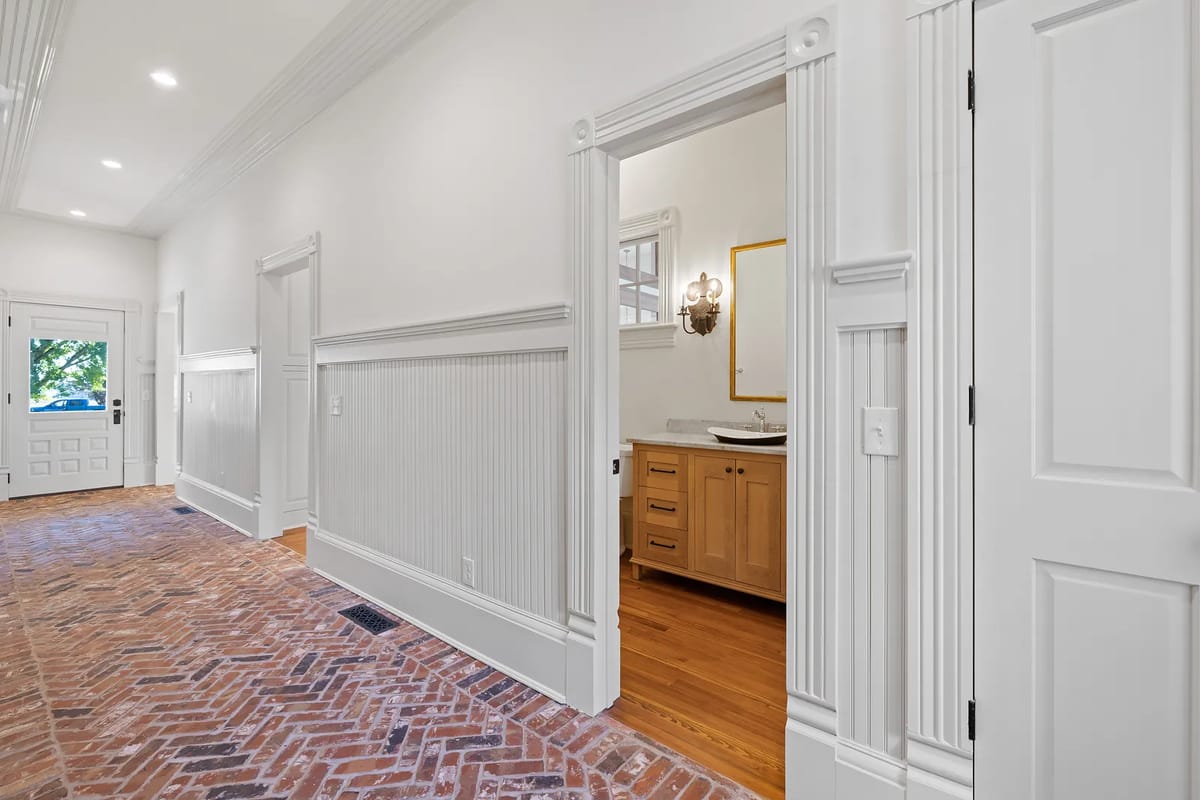 Hallway with brick flooring, wainscoting, doorways, and decorative molding
