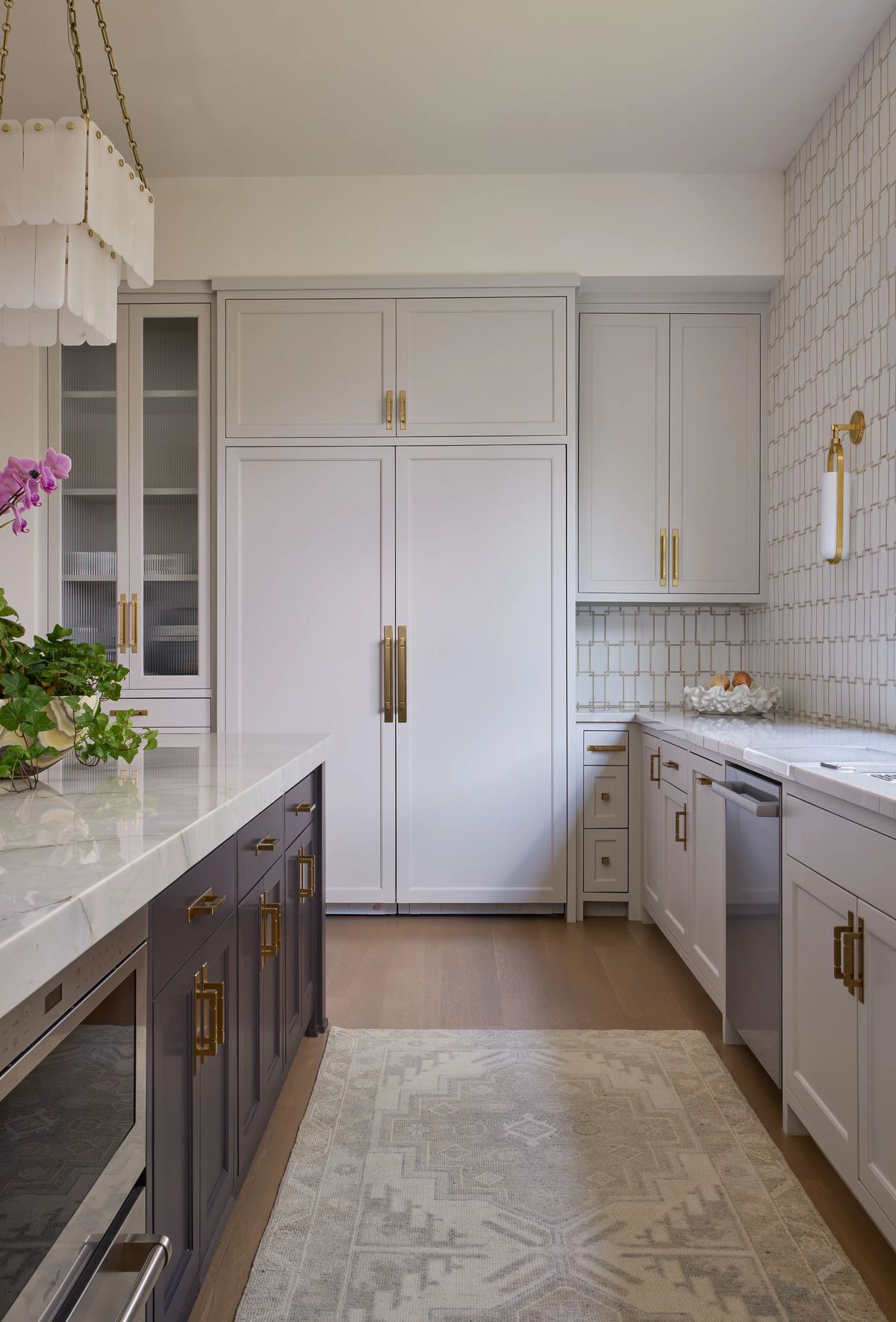 Kitchen with light gray cabinets, marble countertop, backsplash tiles, potted plant, and a decorative rug.