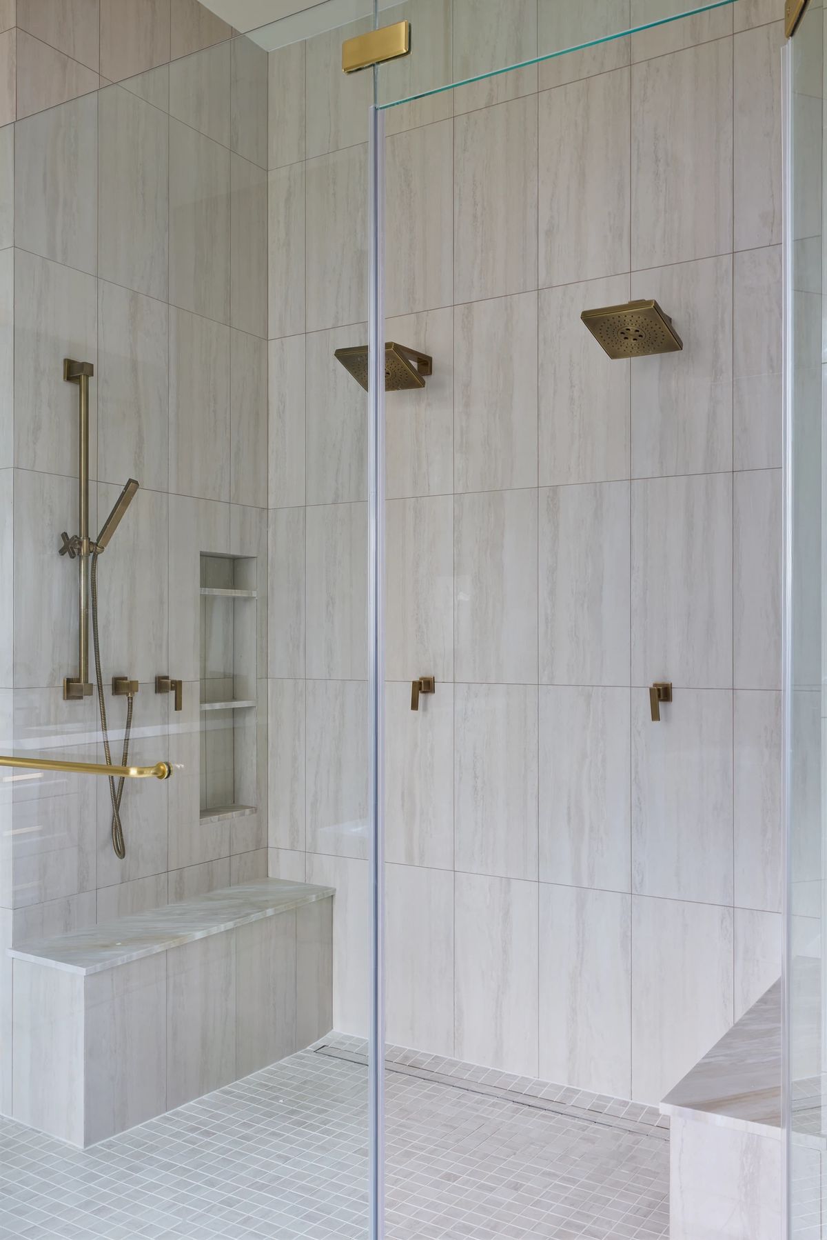 Bathroom with glass shower enclosure, dual showerheads, built-in bench, and light-colored wall tiles