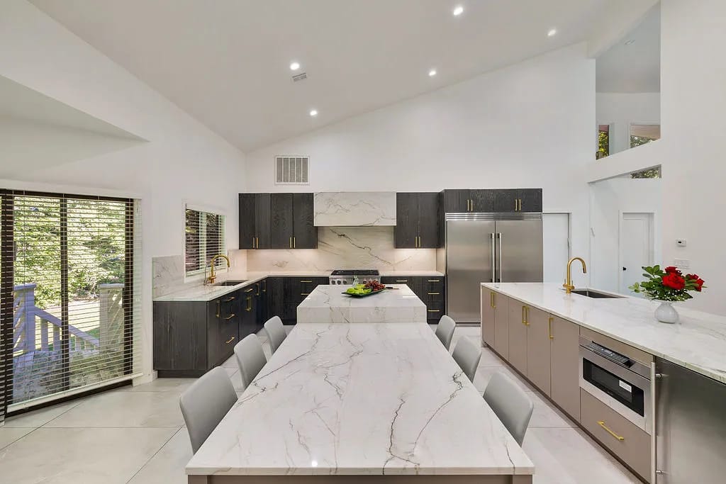 Kitchen with dark wood cabinetry, marble countertops, large island, stainless steel appliances, and large windows.