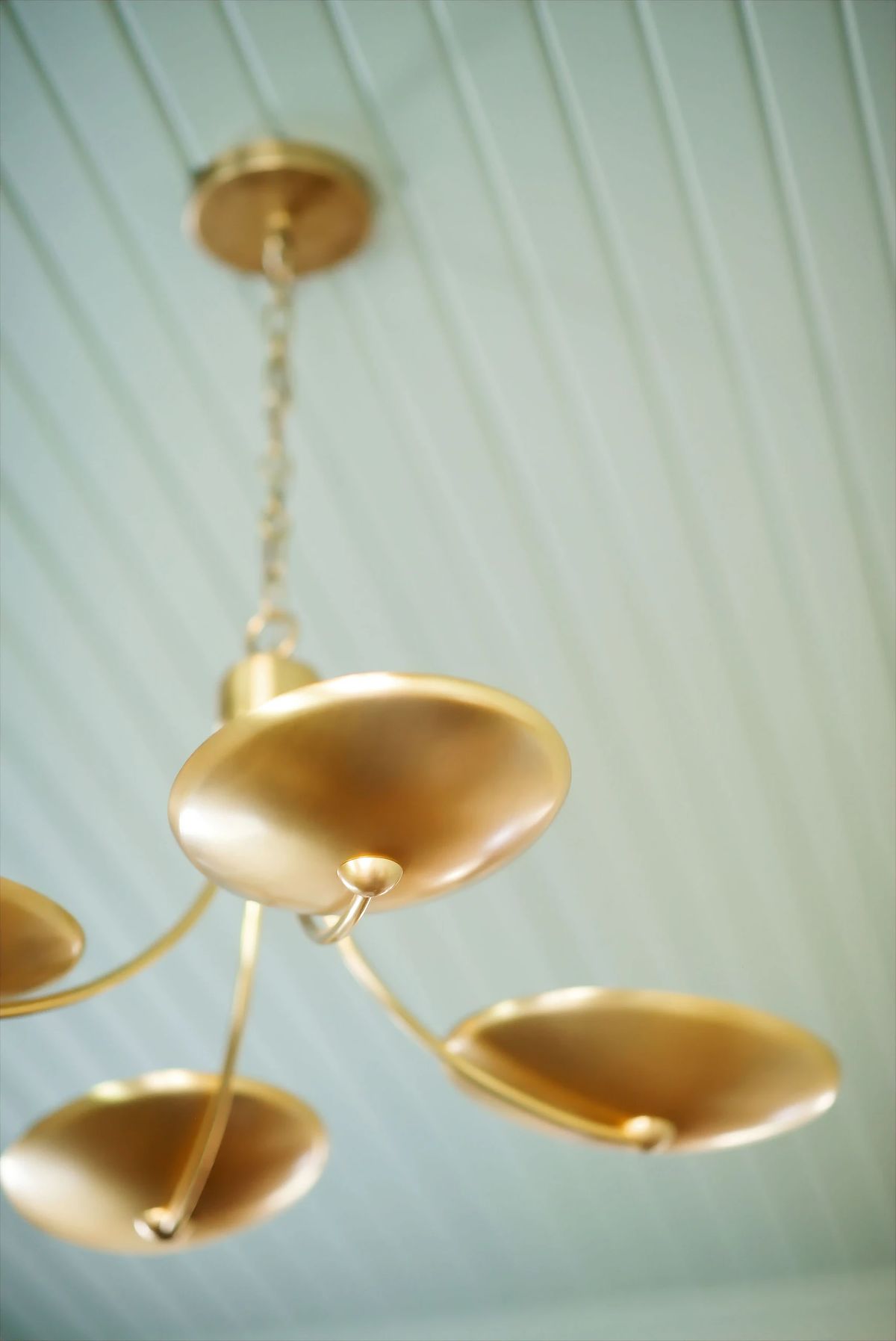 Close-up of a gold chandelier with four circular elements and a white beadboard ceiling.