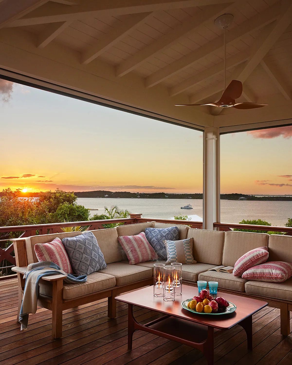 Deck with sectional sofa, coffee table, candles, and fruit bowl with sunset view.