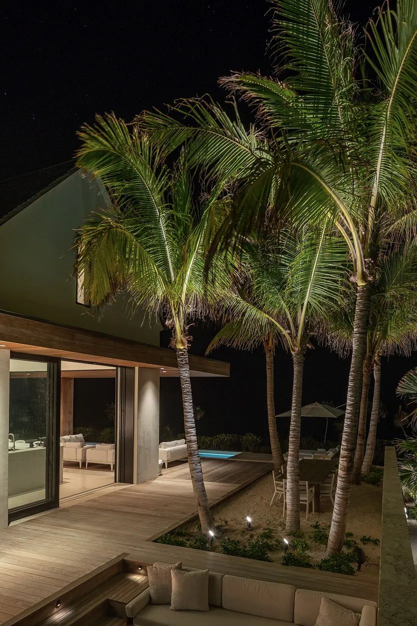 Outdoor deck with seating area, pool, dining table, and palm trees.