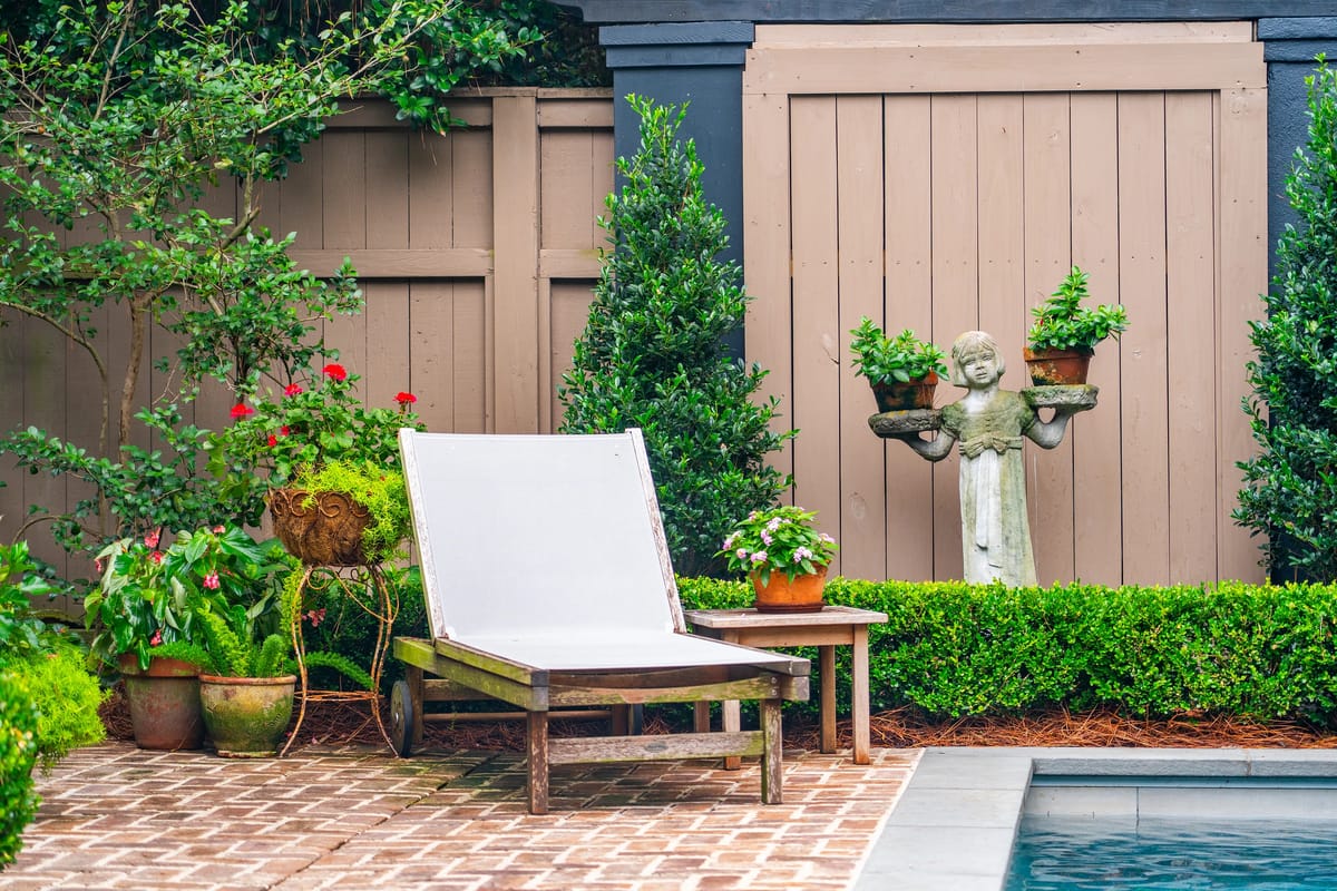 Garden with white lounge chair, stone patio, potted plants, and a statue holding flower pots.