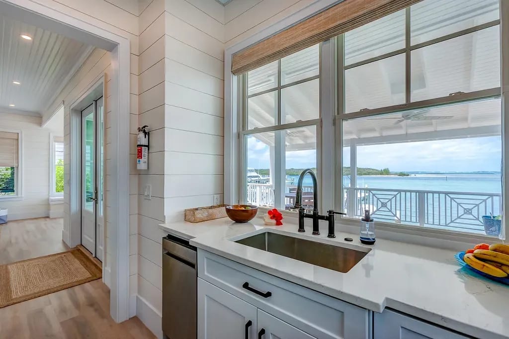 Kitchen with white cabinetry, stainless steel sink, light stone countertop, and large windows for natural light.
