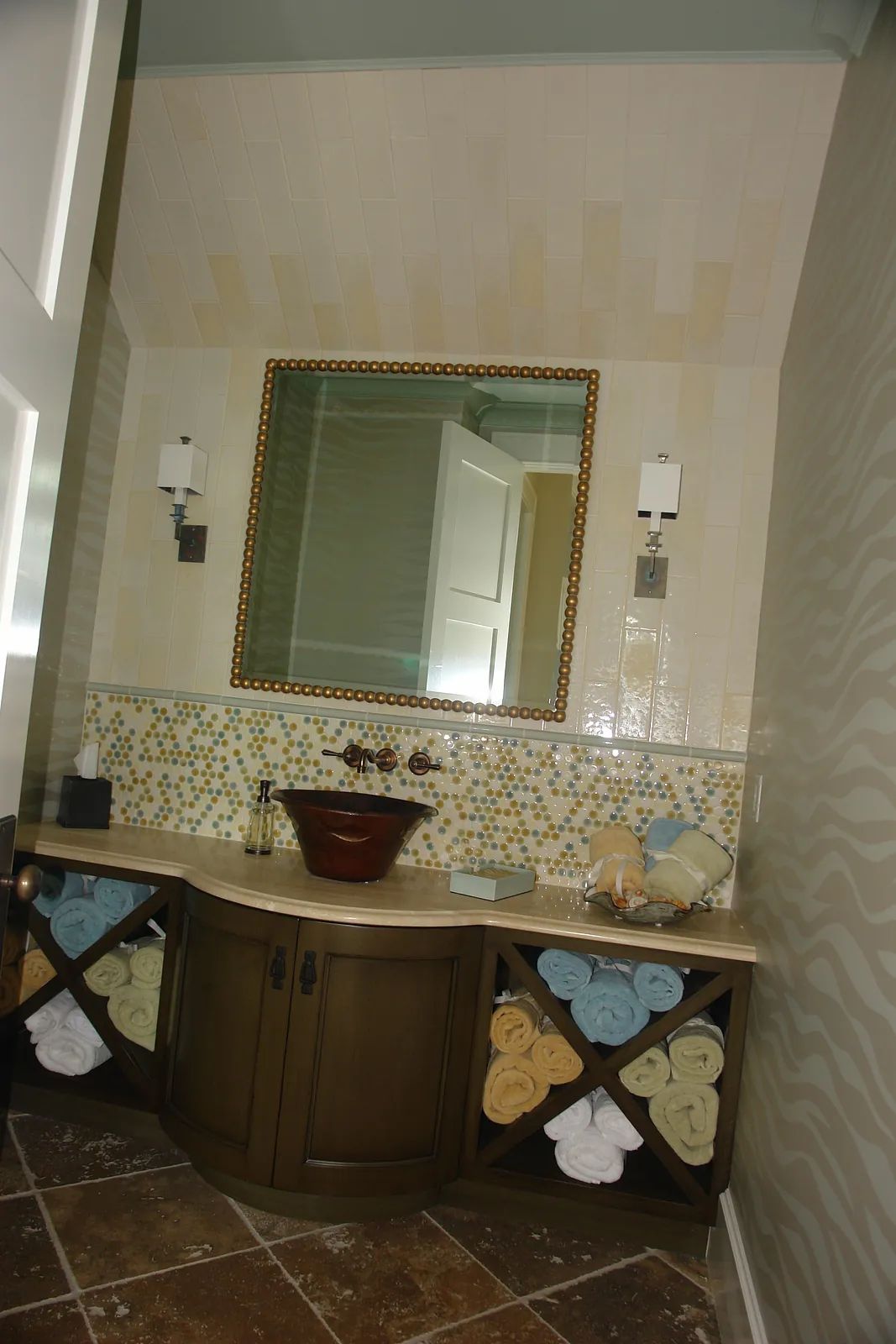 Bathroom with wooden vanity, brown vessel sink, colored tile backsplash, and rolled towels